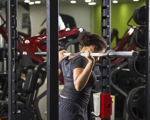 Donna esegue uno split squat con bilanciere nel multipower, concentrata sull'allenamento delle gambe.