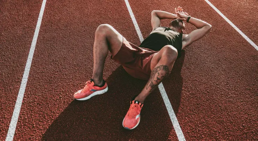 Atleta esausto a terra su una pista da corsa, mani sulla testa. Potrebbe essere il **significato di overtraining**: il corpo che chiede una pausa.