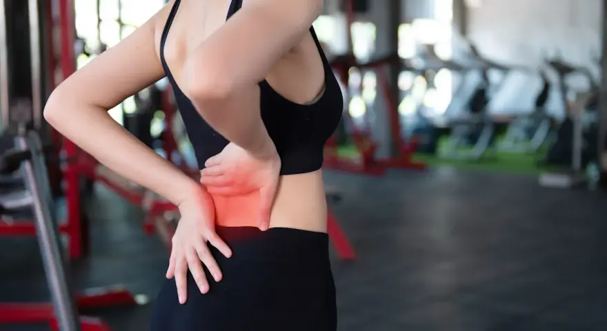 Donna in palestra con le mani sulla schiena, evidenziando il **dolore schiena bassa**.