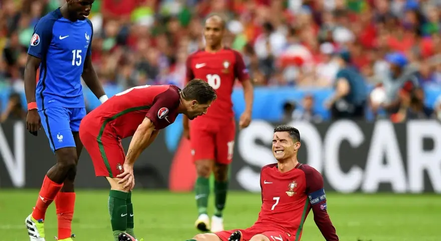 Un giocatore portoghese a terra, forse per un infortunio calcio, mentre un compagno si china preoccupato e un avversario osserva.