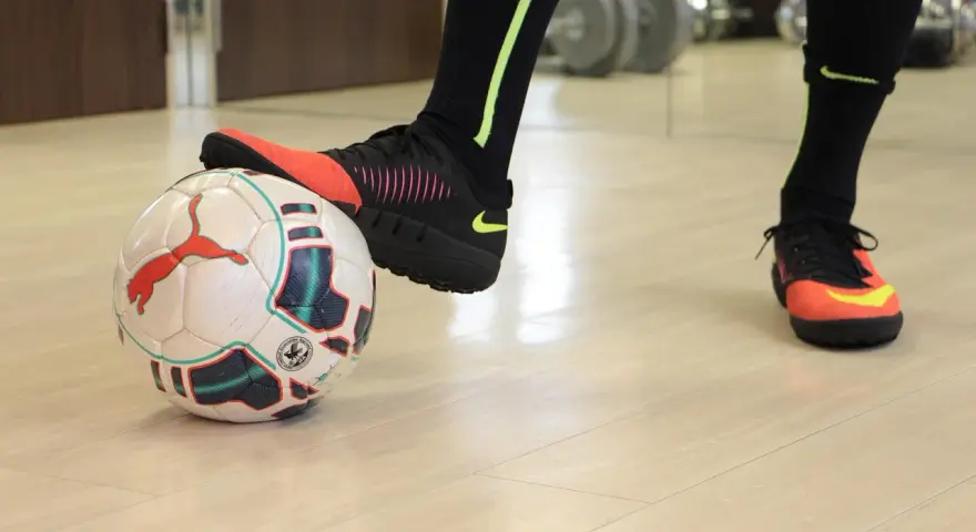 Un giocatore di calcio si prepara a calciare un pallone. Scarpe da calcio arancioni e nere, calzettoni neri con dettagli fluo.