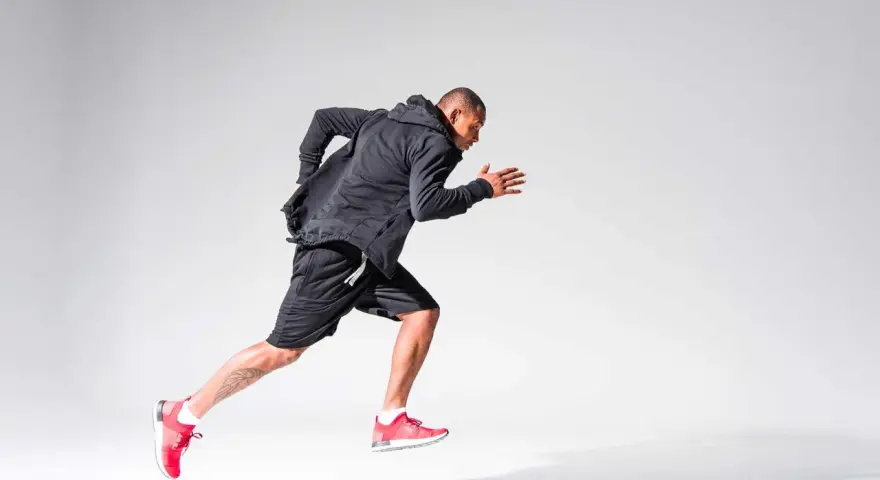 Atleta in corsa, concentrato sul suo obiettivo di aumentare il VO2max. Indossa abbigliamento sportivo nero e scarpe rosse.