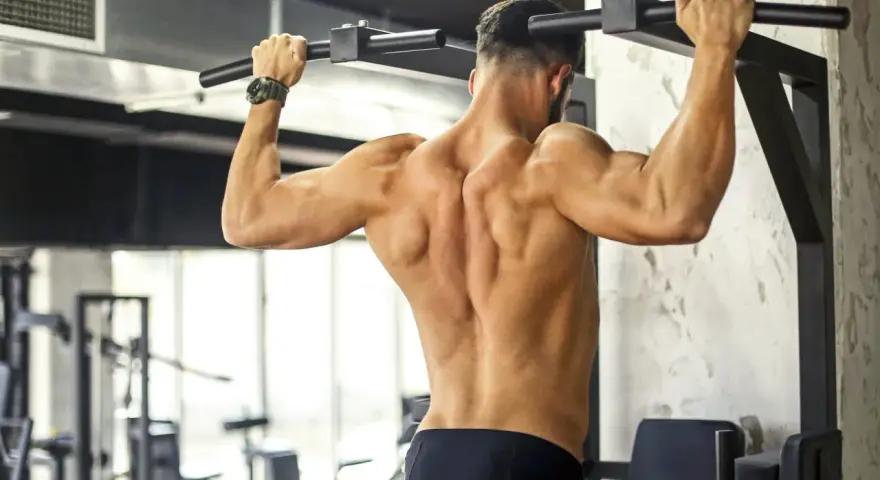 Uomo con muscoli dorsali scolpiti che esegue trazioni alla sbarra in palestra.