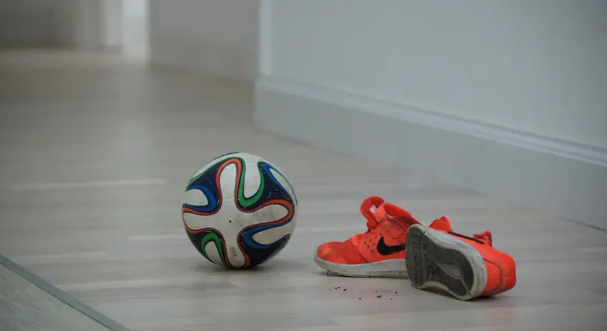 Pallone da futsal e scarpe arancioni su parquet. Pronto per una partita, ma cos'è il futsal? Uno sport veloce e tecnico.