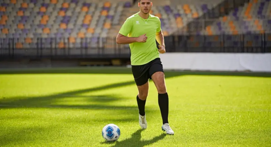 Giovane calciatore corre sul campo verde, allenando la resistenza. Un pallone da calcio è vicino a lui.