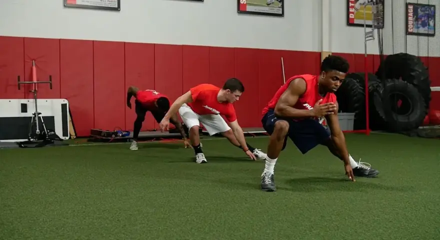 Giovani atleti in allenamento corsa calcio, eseguono esercizi di stretching e agilità su un campo sintetico.