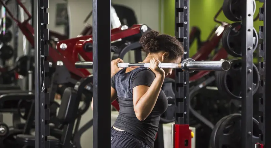 Donna esegue uno split squat con bilanciere nel multipower, concentrata sull'allenamento delle gambe.