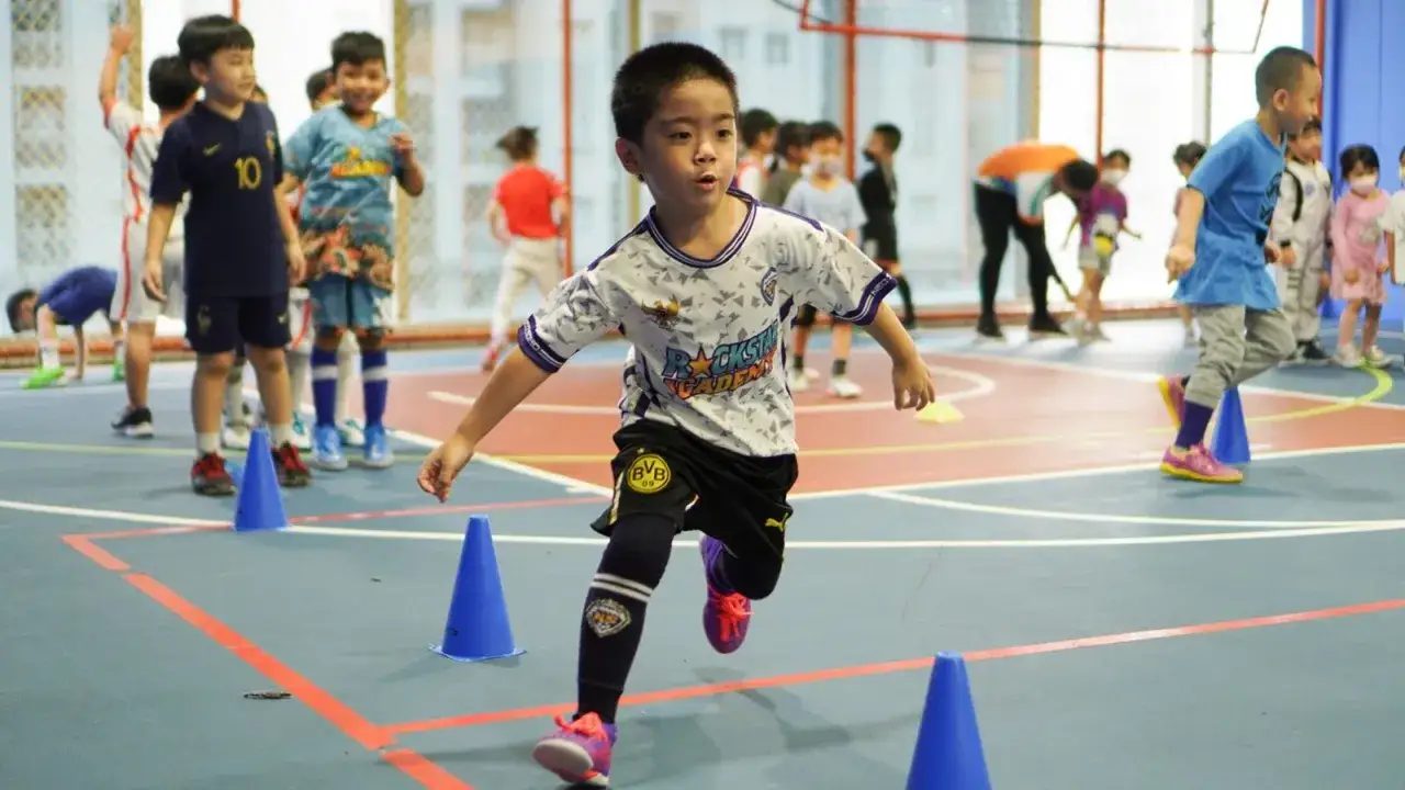 Bambini in allenamento, un percorso a ostacoli con coni blu. Un ragazzo corre, impegnato nel suo lavoro metabolico, con il calcio come passione.