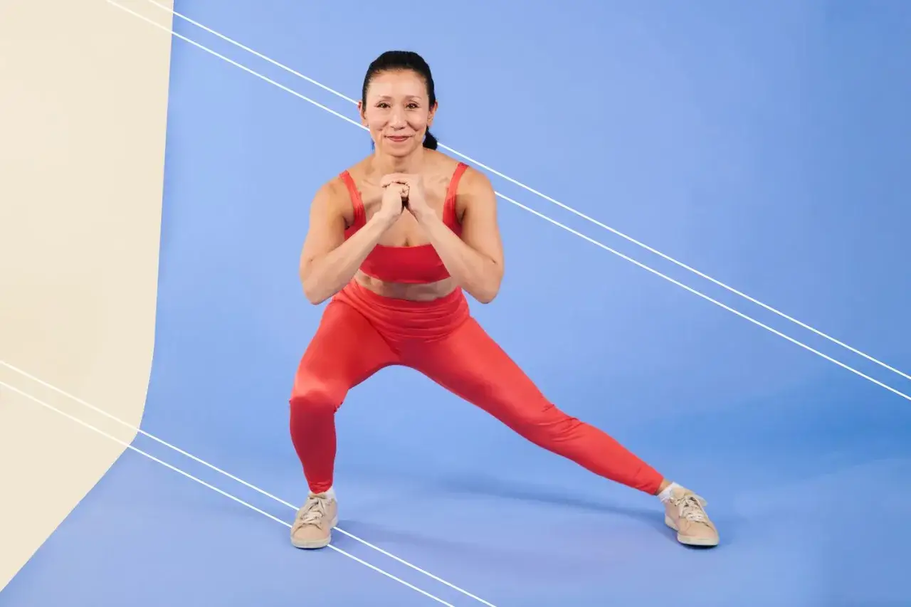 Donna in tenuta sportiva rossa esegue uno squat laterale, allenando i muscoli della gamba anteriore.
