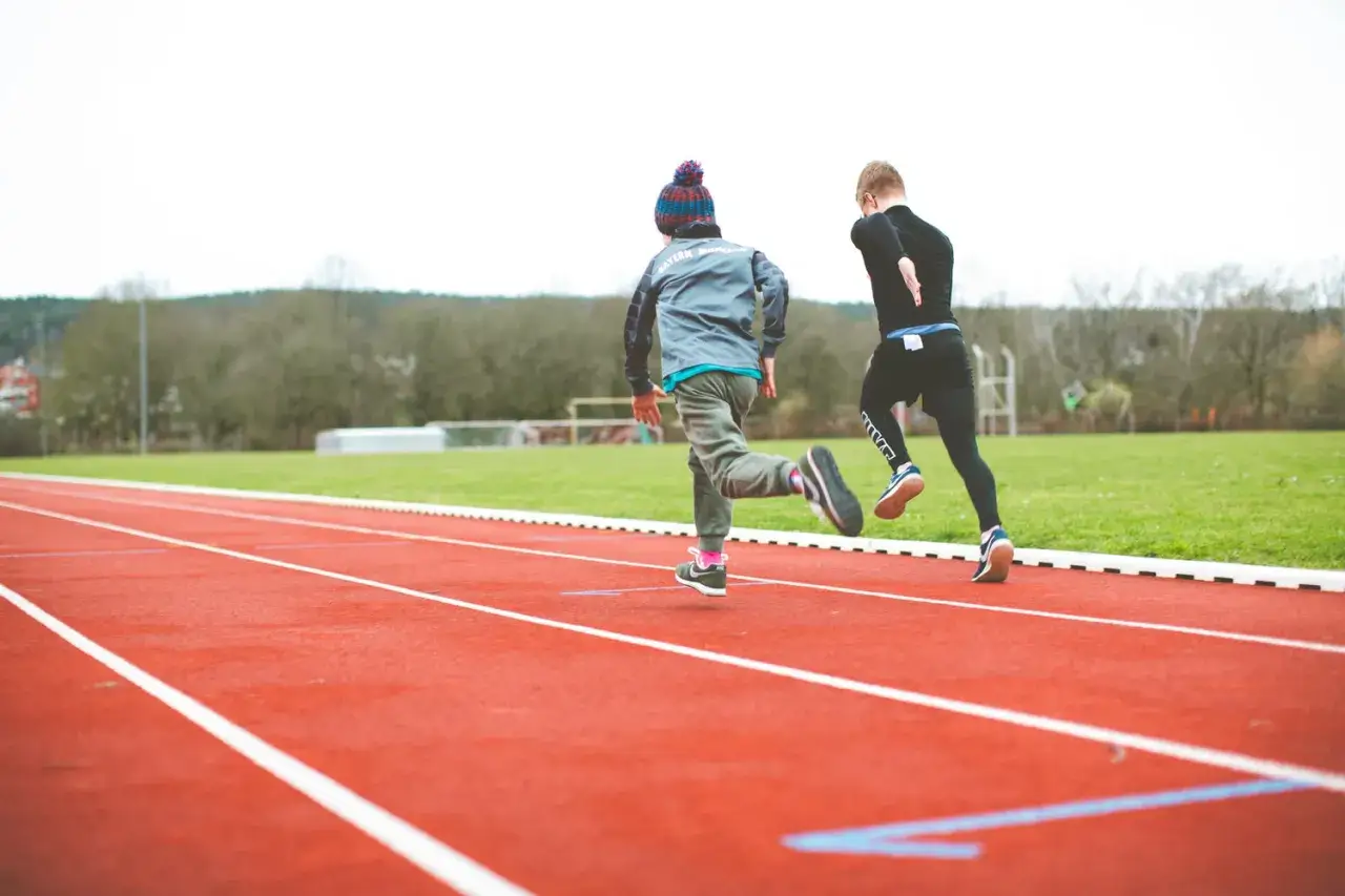 Due ragazzi corrono su una pista rossa, impegnati in un test di cooper scolastico.