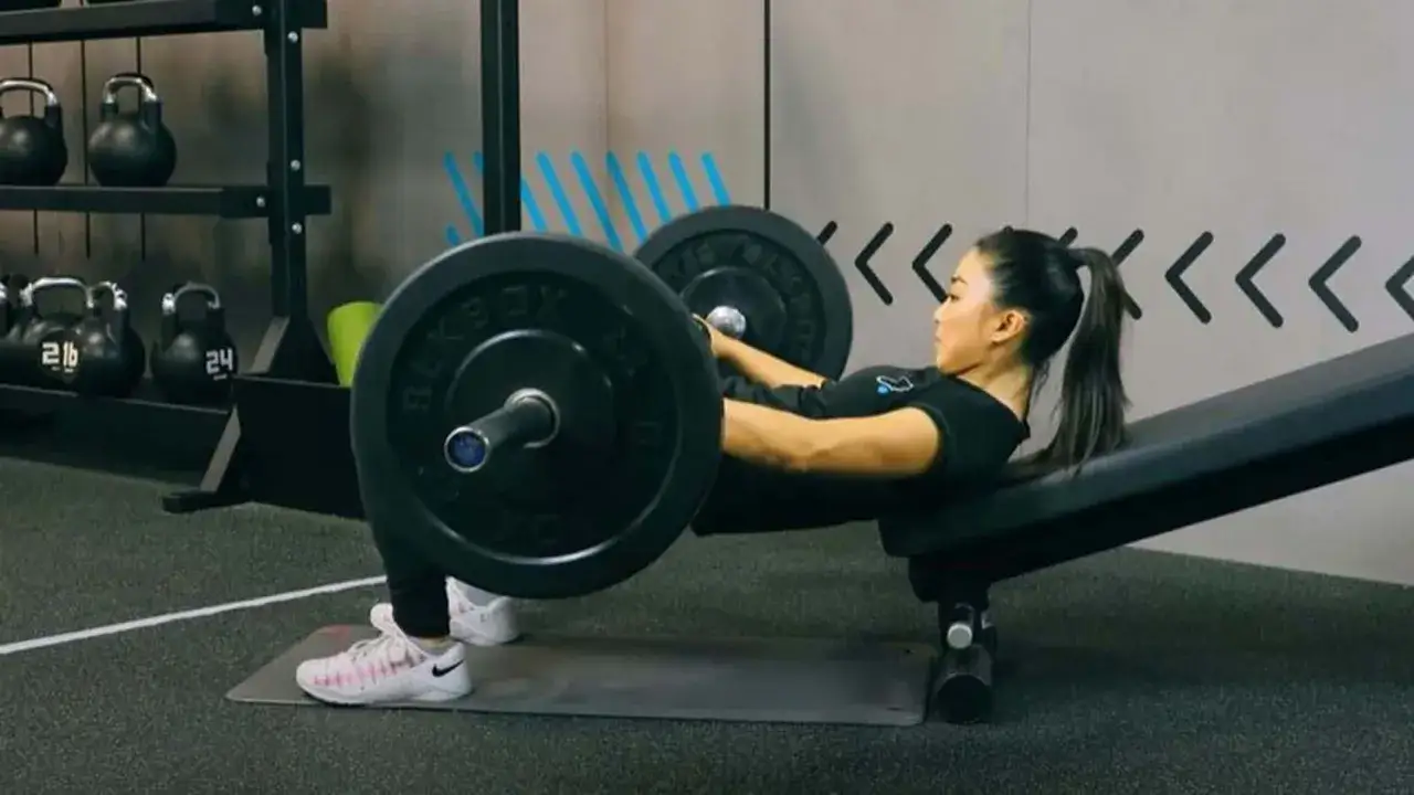 Donna esegue hip thrust con bilanciere su panca, un esercizio efficace per i glutei. I benefici sono notevoli per forza e forma.