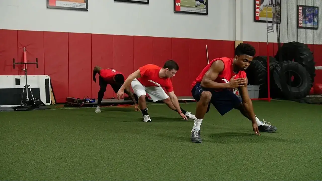 Giovani atleti in allenamento corsa calcio, eseguono esercizi di stretching e mobilità articolare su un campo sintetico.