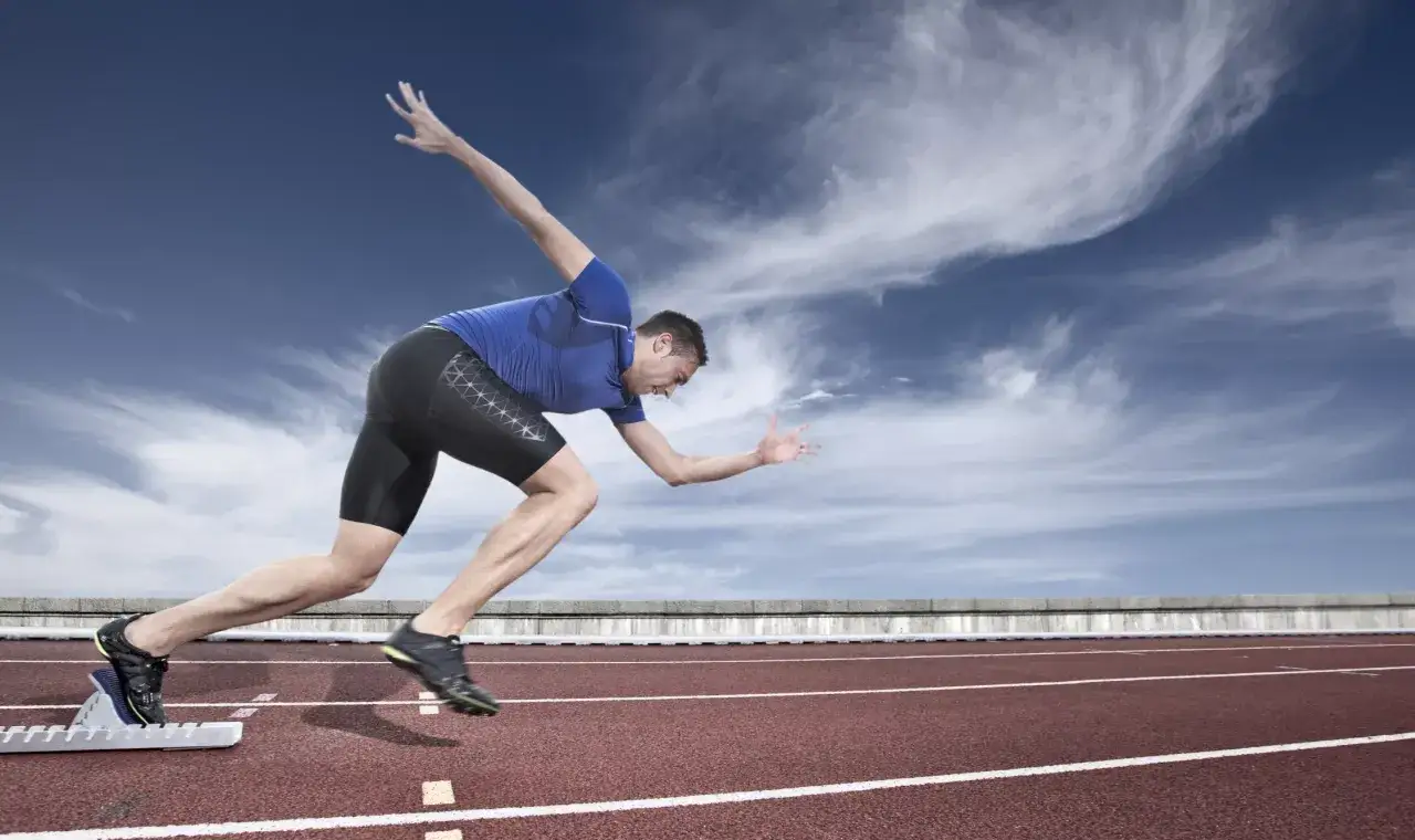 Atleta in partenza dai blocchi, pronto a dimostrare la sua repeated sprint ability su una pista di atletica sotto un cielo nuvoloso.