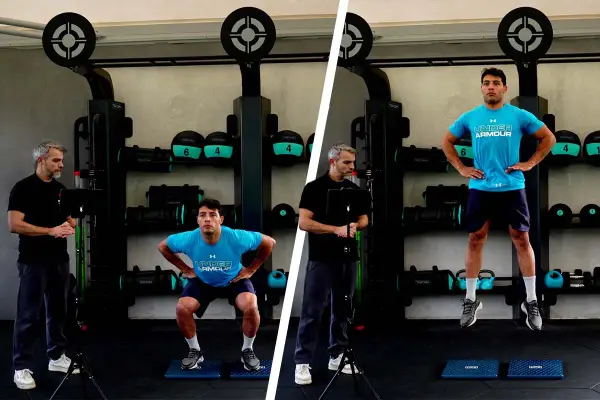 Uomo esegue un countermovement jump in palestra, guidato da un istruttore.